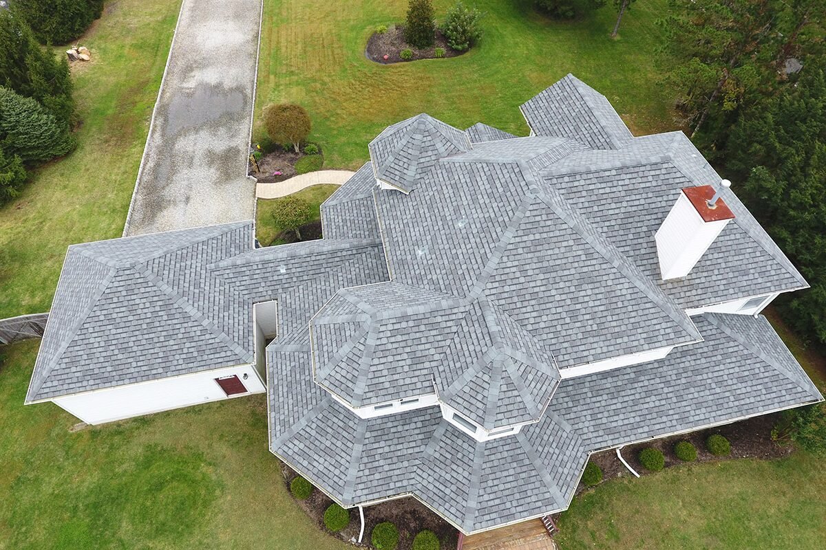 Aerial view of a very large home in Monmouth County NJ, featuring an intricate, multi-level gray shingle roof, showcasing the complexity and precision of our roofing installation services.